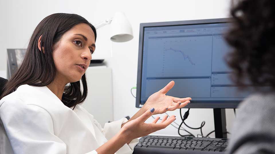 Profissional de cuidados auditivos explicando resultados de um teste auditivo exibido na tela do computador.