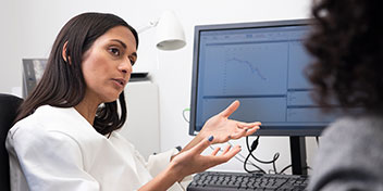 Profissional de saúde auditiva explicando resultados de um teste auditivo em um computador para um paciente.