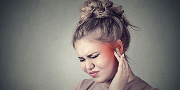 Uma pessoa ajusta um aparelho auditivo discreto em uma das orelhas, destacando o cuidado com a audição. O fundo é neutro, criando foco no dispositivo auditivo.