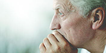 Uma orelha de um idoso em destaque, sugerindo o uso de aparelhos auditivos. O fundo é desfocado, transmitindo um ambiente calmo, possivelmente num centro auditivo