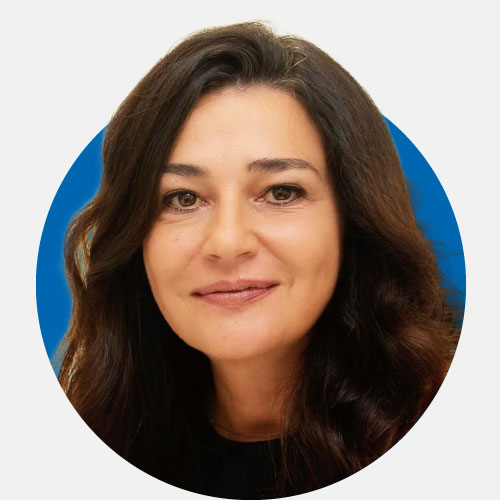 Audiologista com cabelos castanhos ondulados e fundo azul.