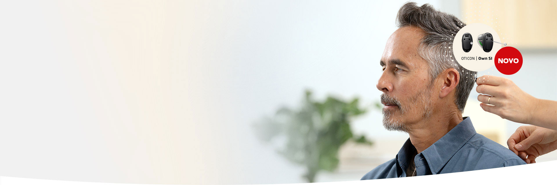 Aparelho auditivo Oticon Own SI sendo ajustado na orelha de um homem sentado. Fundo com planta desfocada, destaque para o texto ’OTICON Own SI’ e selo ’NOVO’.