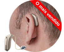 Aparelho auditivo bege posicionado atrás da orelha de um homem, com discreto receptor no canal auditivo. Texto no topo em vermelho: ’O mais vendido’. Contexto neutro.