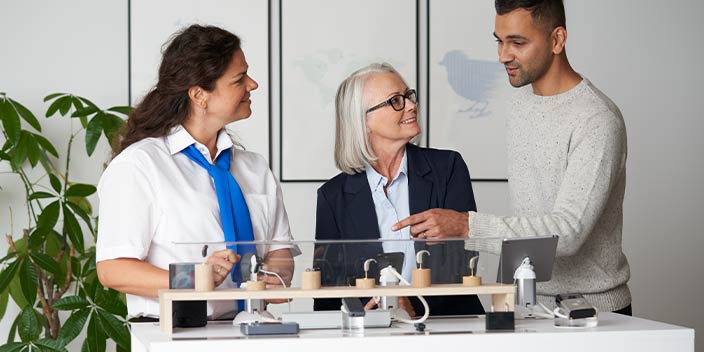 Audioprothésiste expliquant des accessoires pour appareils auditifs à deux clients