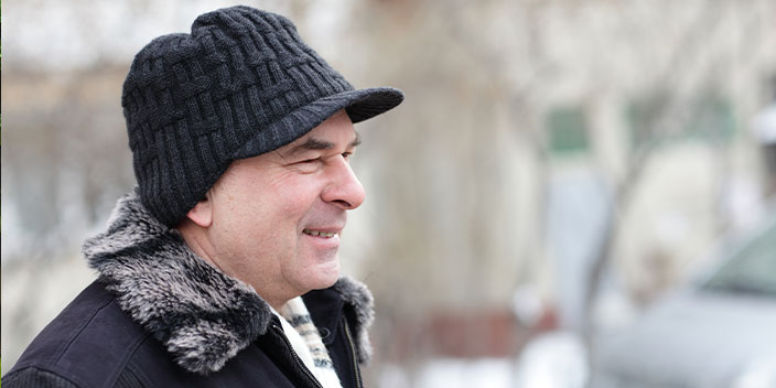 Homme portant un bonnet en tricot et une veste en hiver, sur un fond de paysage enneigé flou.