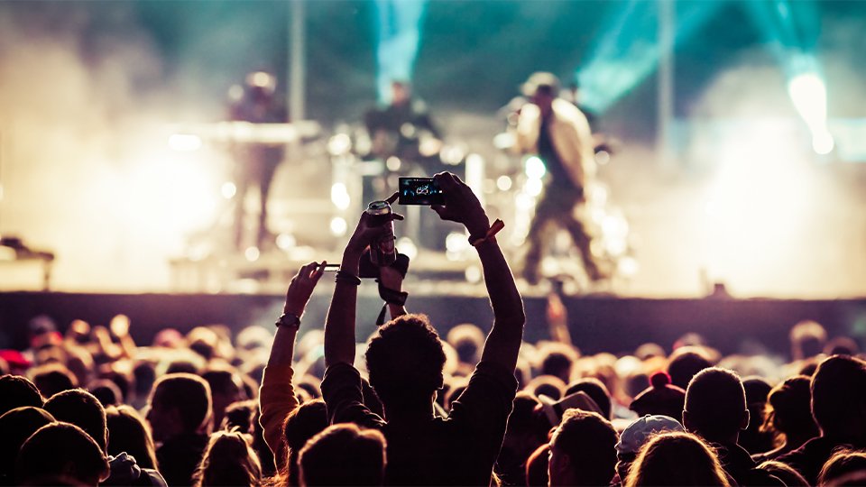 Foule profitant d’un concert avec des lumières vives et une personne tenant un smartphone pour capturer l’instant.