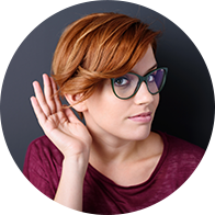 Une femme aux cheveux roux tenant une main près de son oreille, illustrant l'écoute ou une perte auditive.