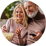 Un couple assis sur un canapé partage un bol de pop-corn tout en tenant une télécommande.