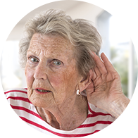 Une femme âgée en chemise rayée rouge et blanche place sa main près de son oreille, indiquant un effort pour mieux entendre.