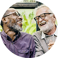 Deux hommes conversant dans un environnement extérieur lumineux, avec un verre d’eau à la main d’un des hommes.