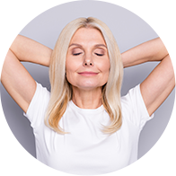 Une femme blonde souriante portant un t-shirt blanc, les mains derrière la tête.