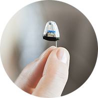 Une main tient un appareil auditif discret et miniature.