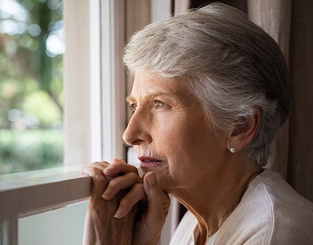 Femme senior aux cheveux gris regardant par une fenêtre en plein jour.