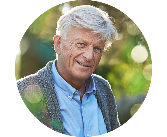 Un homme âgé sourit à l’extérieur.