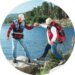 Ein älteres Paar hilft sich gegenseitig beim Wandern entlang eines Flusses.