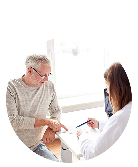 Ein Mann mittleren Alters zeigt auf ein Dokument, während eine Hörakustikerin in weissem Kittel mit Stift Notizen macht; im Hintergrund ein helles, modernes Hörzentrum.