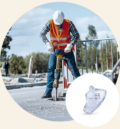 Ein Bauarbeiter in Warnweste und Helm bedient einen Presslufthammer auf einer Baustelle im Freien. Im Vordergrund wird ein Gehörschutz-Otoplastik dargestellt, ideal zur Lärmschutzprävention.