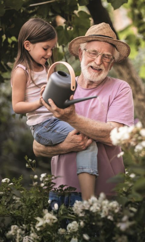 Ein Großvater mit seiner Enkeltochter beim Blumen gießen im Garten