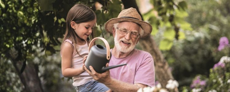 Ein Großvater mit seiner Enkeltochter beim Blumen gießen im Garten