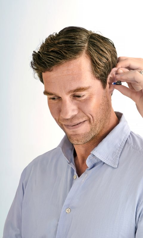 Ein junger Mann bekommt das Oticon Zeal Hörgerät in sein Ohr eingesetzt