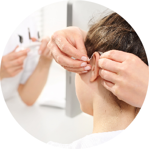 Akustiker setzt einer jungen Kundin ein Hörsystem in das Ohr ein