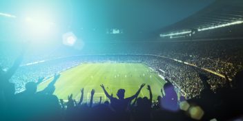 Fodboldstadion med fodboldkamp og heppende fans. Det er mørkt, og der er kunstigt lys på banen.