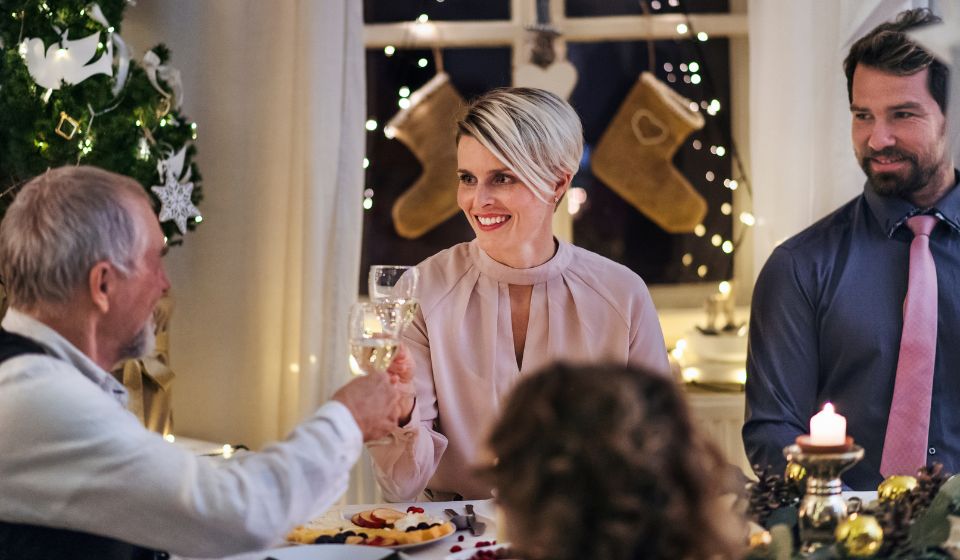 Kvinde og mand skåler ved julebordet. Der er pyntet op og levende lys. 