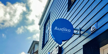 Audikas blå skilt på siden af en bygning under en blå himmel