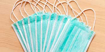 Grønne engangsmundbind med hvide elastikker er spredt ud i en vifteform på en lys træoverflade. Ingen tekst fremgår, og billedet relaterer ikke til høreklinikudstyr.