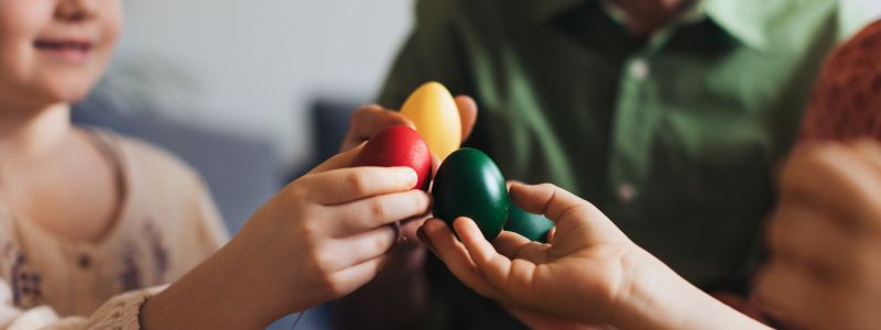 En mand og to børn holder deres malede påskeæg op mod hinanden. 