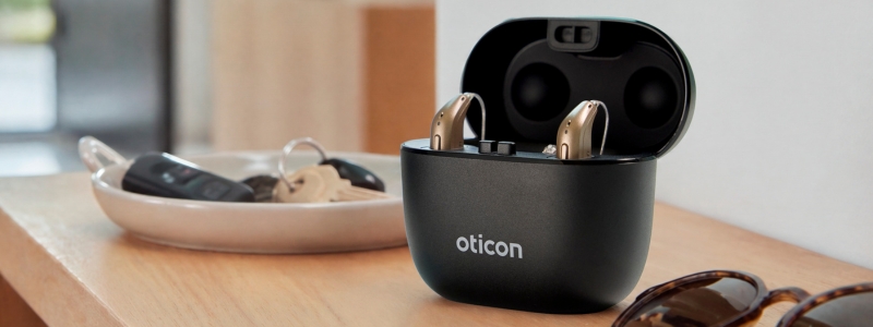 Et sæt Oticon Reveal står i opladeren på en kommode ved siden af en skål med nøgler og diverse andre ting. 