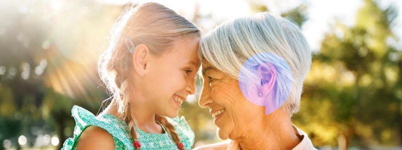Pige og ældre kvinde har panden mod hinanden og smiler. De er udenfor, og solen skinner.  