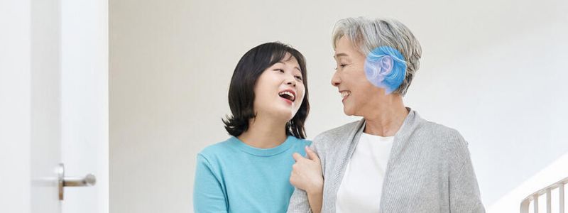 Teenagepige og ældre kvinde - begge af asiatisk udseende - går arm i arm indenfor, mens de smiler. 