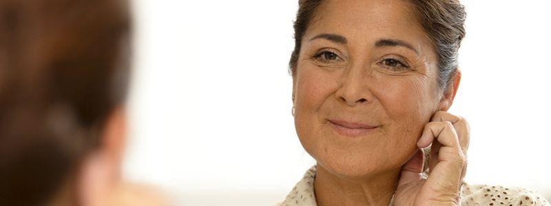 En mørkehåret, moden kvinde ser sig i spejlet tæt på. Hun smiler til sit spejlbillede.