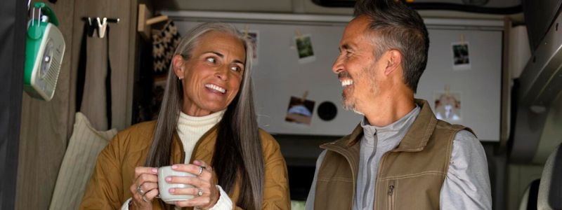 Kvinde og mand står og drikker kaffe i deres autocamper.