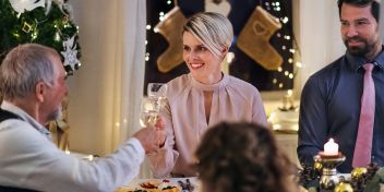 Kvinde og mand skålet ved et pyntet julebord. Der er levende lys og pyntet op i rummet. 