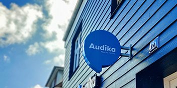 Audikas blå skilt på siden af en bygning under en blå himmel