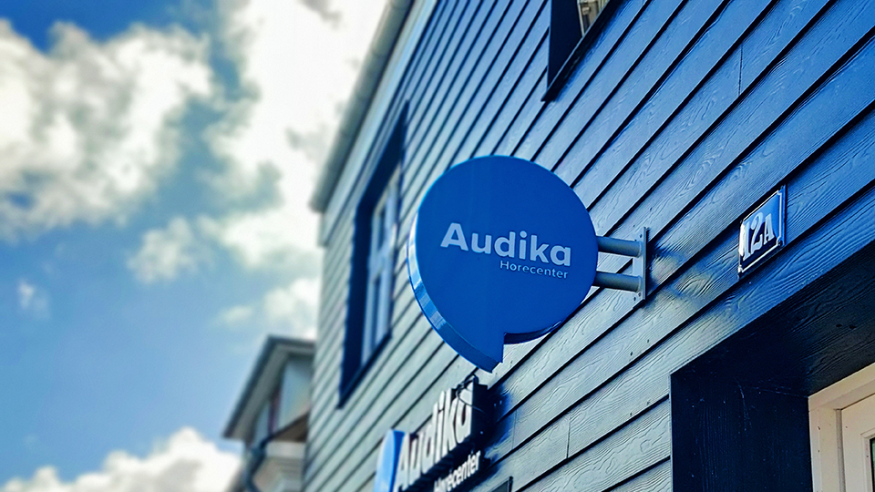 Audika Hørecenter-skilt på en blå bygning under en klar himmel