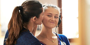 Mor kysser datter på kinden, mens datteren har høretelefoner på.