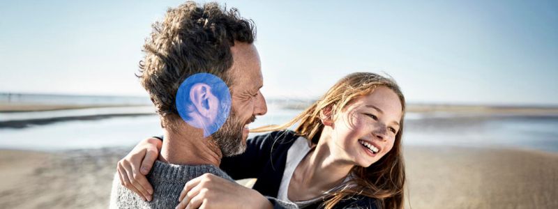 Mand og pige er på stranden. Han holder pigen i sine arme og smiler til hende.