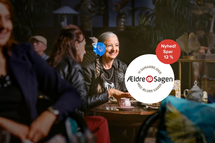 To personer samtaler ved et bord med te i en hyggelig, dæmpet belysning. Tekst på billedet inkluderer: ’Vi samarbejder med Ældre Sagen’ og ’Nyhed! Spar 12 %’.