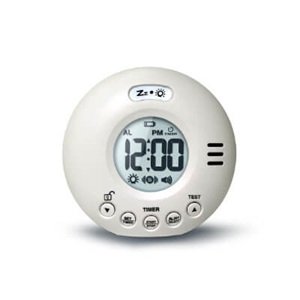 Hvidt digitalt vækkeur med rund form viser klokken 12:00 på en skærm med store tal. Knapper nederst inkluderer ’TIMER’ og ’TEST.’ Designet har alarmlogo og højtaler.