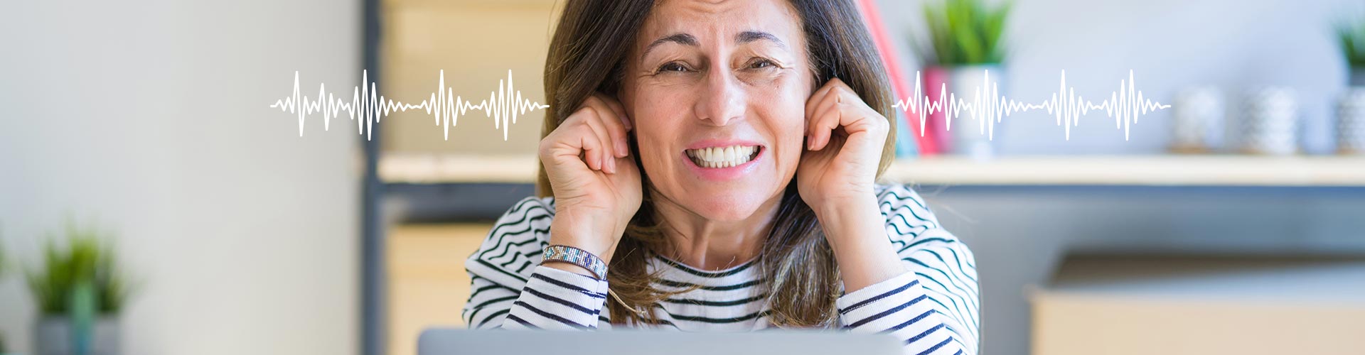 En kvinde i stribet trøje holder fingrene ved ørerne med lydbølger illustreret ved siden af. Baggrunden viser en lys indendørs setting med planter og hylder i et kontorlignende miljø.