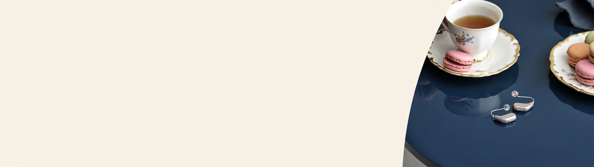 Høreapparater fra Oticon placeret på et blåt bord ved siden af fine teselskabsmotiver med macarons og te.