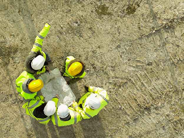 Håndværkere med sikkerhedshjelme og refleksjakker gennemgår byggeplaner på en byggeplads