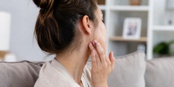 Mujer tocándose la zona de la parótida por inflamación causada por paperas o parotiditis
