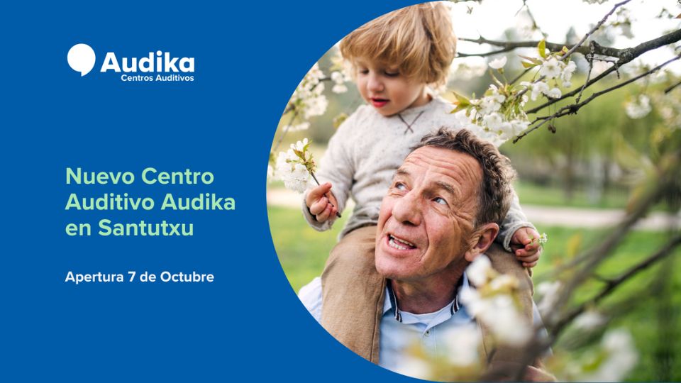 Un padre carga a su hijo en los hombros junto a un árbol florecido en un parque. A la izquierda, sobre un fondo azul, texto promocional: **’Audika Centros Auditivos. Nuevo Centro Auditivo Audika en Santutxu. Apertura 7 de Octubre’**.