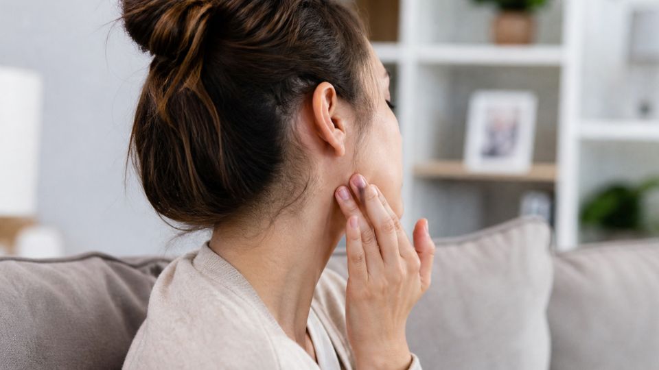 Mujer tocándose la zona de la parótida por inflamación causada por paperas o parotiditis