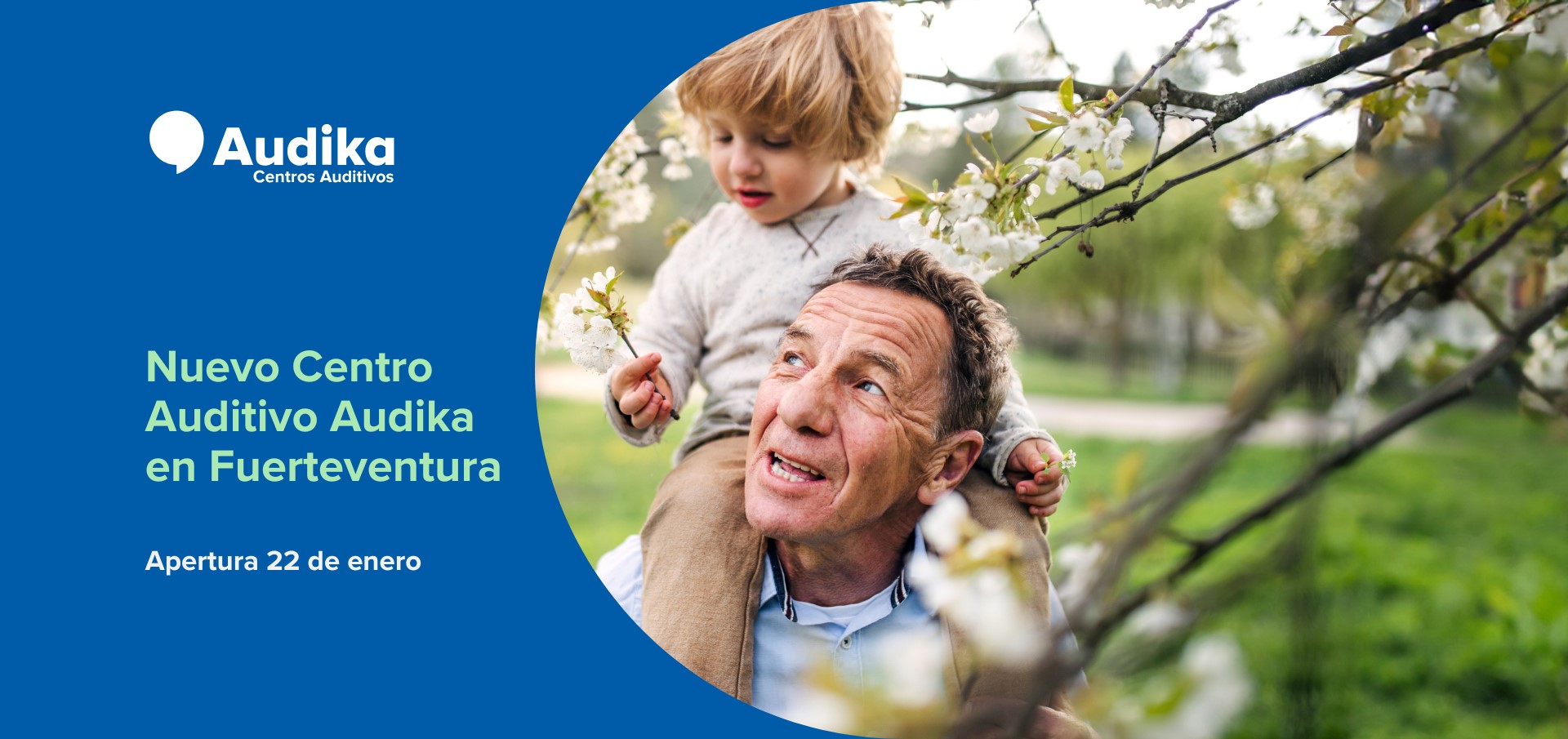 Logo de Audika Centros Auditivos a la izquierda sobre fondo azul. Texto: ’Nuevo Centro Auditivo Audika en Fuerteventura. Apertura 22 de enero’. A la derecha, padre y niño entre árboles florecidos.