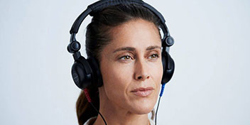 Una persona usa audífonos grandes negros conectados, probablemente durante una prueba auditiva en un entorno clínico o de diagnóstico auditivo.